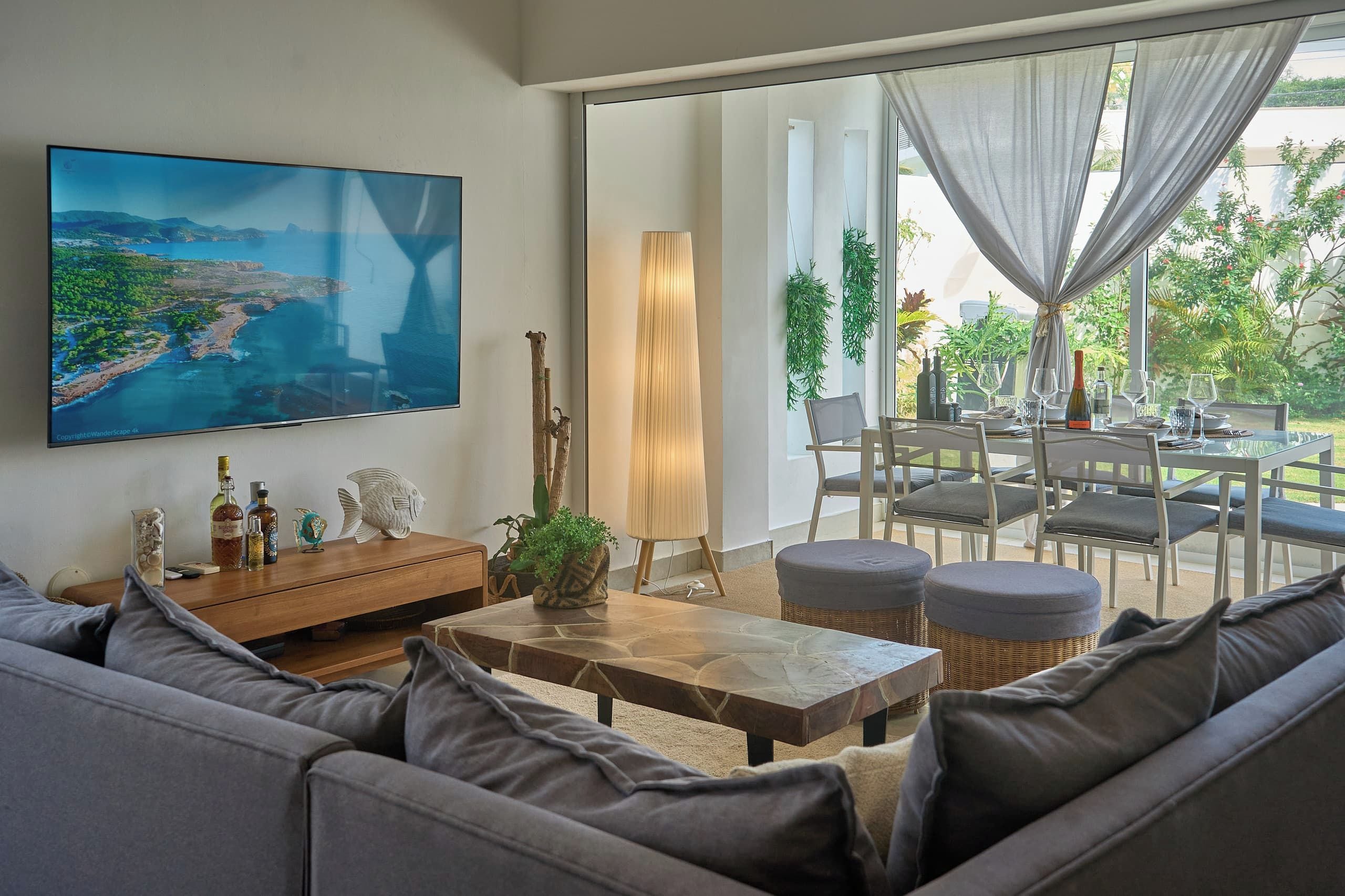 Una sala moderna con un televisor de pantalla plana grande, un sofá, una mesa de centro y un comedor con sillas y una mesa dispuesta para dos.