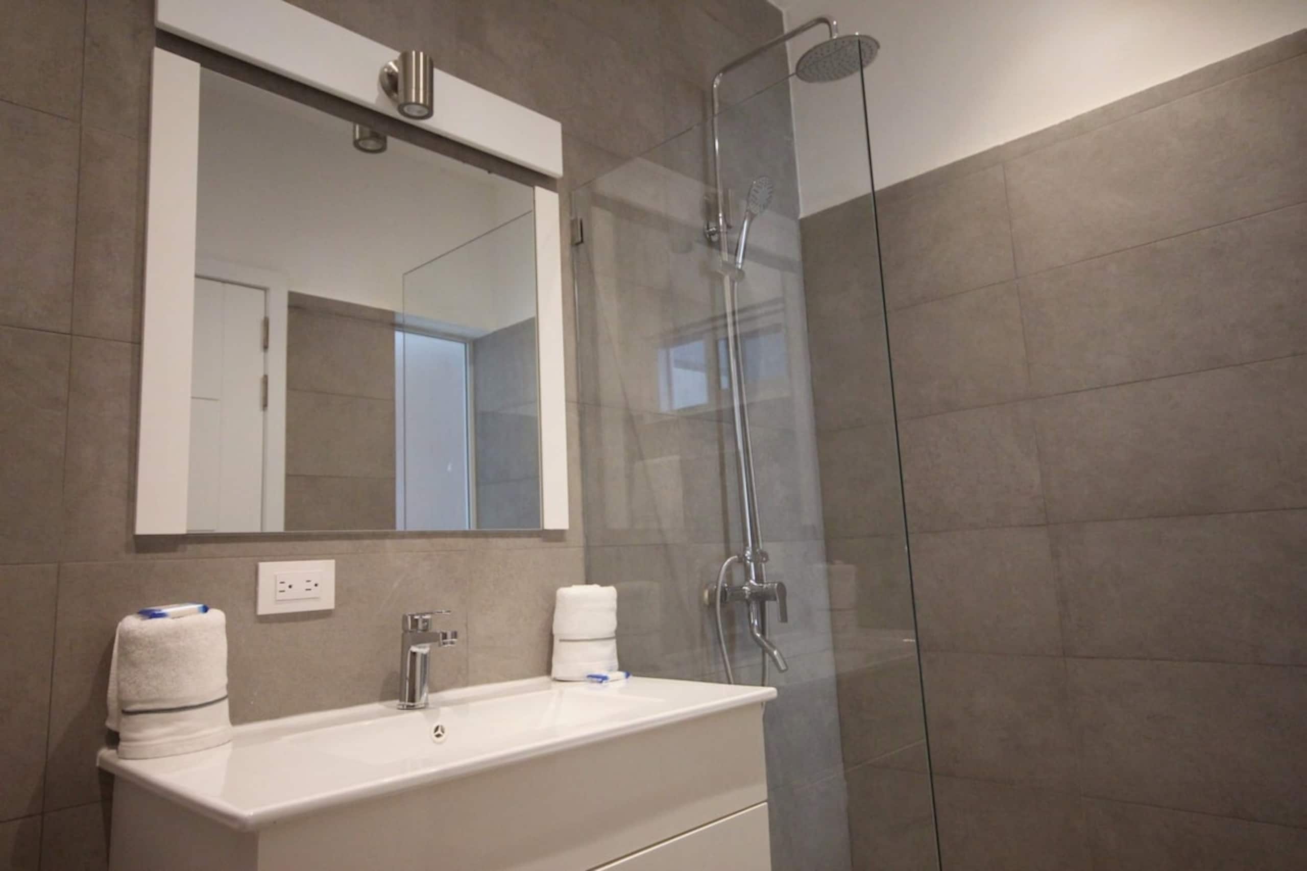 A modern bathroom with a glass-enclosed shower, a white sink, and a mirror above it.