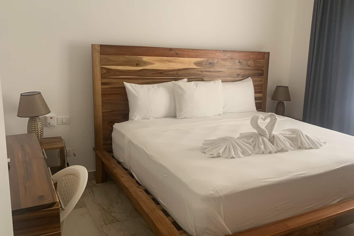 Habitación de hotel con cabecera de madera, ropa de cama blanca y una decoración con toalla en forma de corazón.
