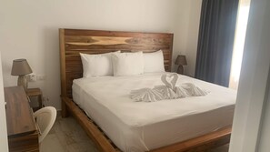 Habitación de hotel con cabecera de madera, ropa de cama blanca y una decoración con toalla en forma de corazón.