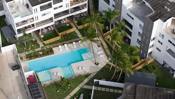 A modern residential building with a rooftop pool, surrounded by palm trees and a fenced garden area.