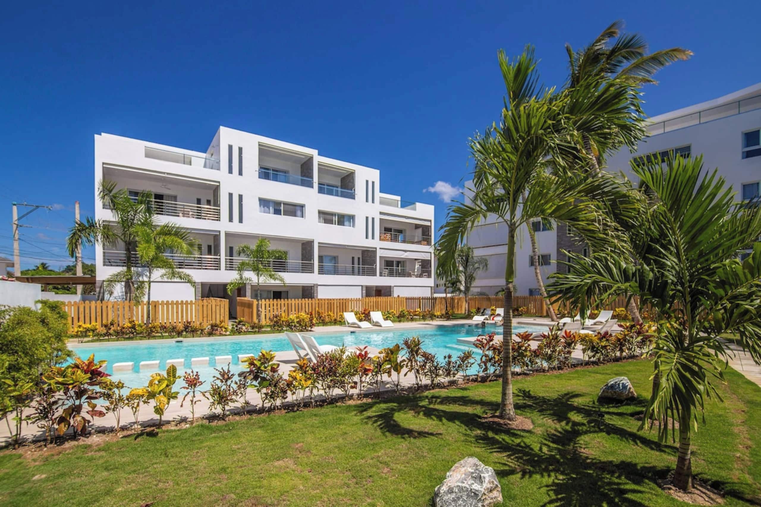 Un hotel moderno de varios pisos con piscina, palmeras y cerca de madera.