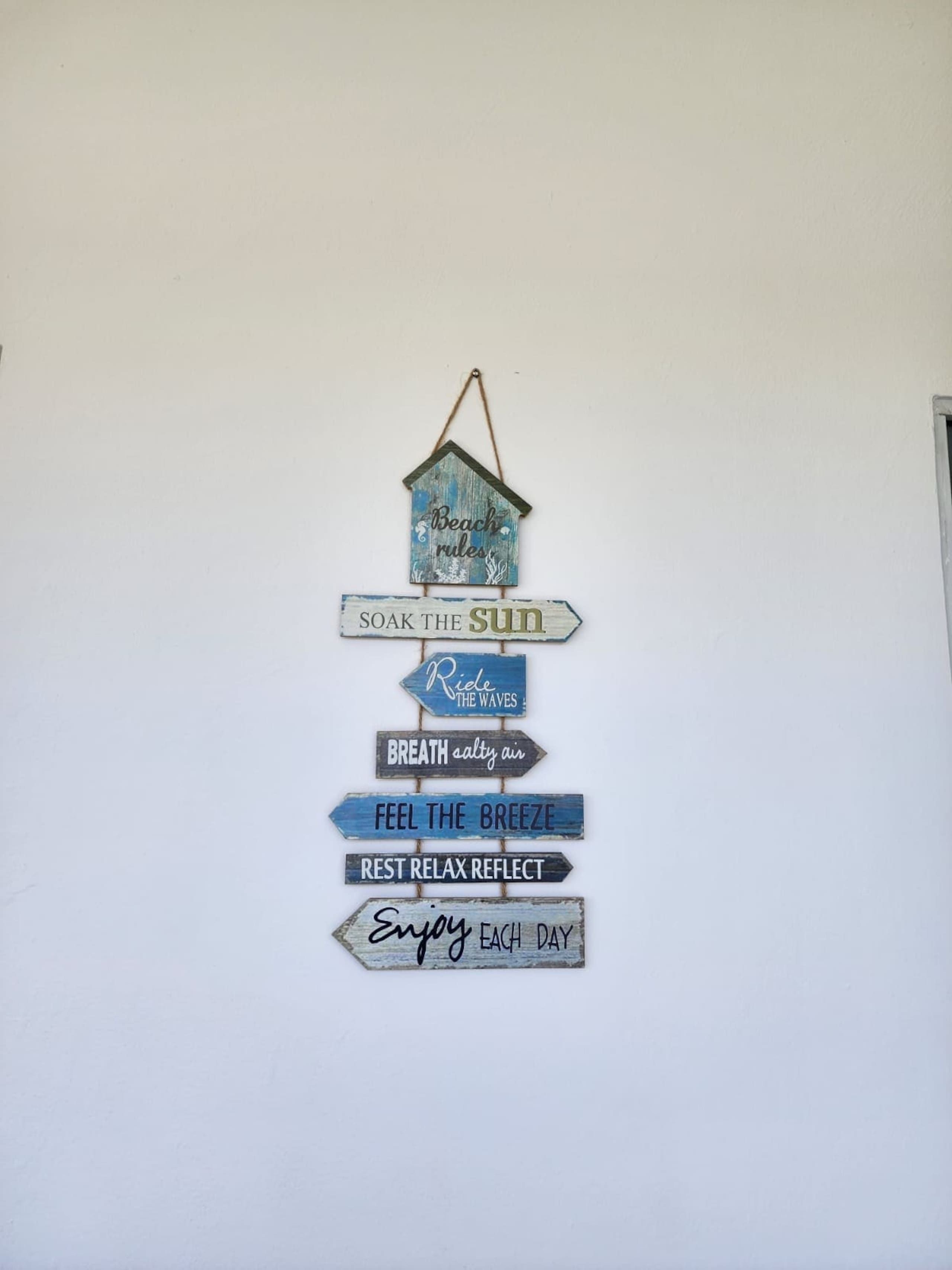A wall with a wooden sign hanging from the ceiling, featuring various phrases related to relaxation and enjoying nature.