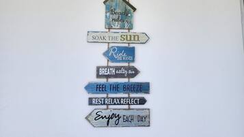 A wall with a wooden sign hanging from the ceiling, featuring various phrases related to relaxation and enjoying nature.