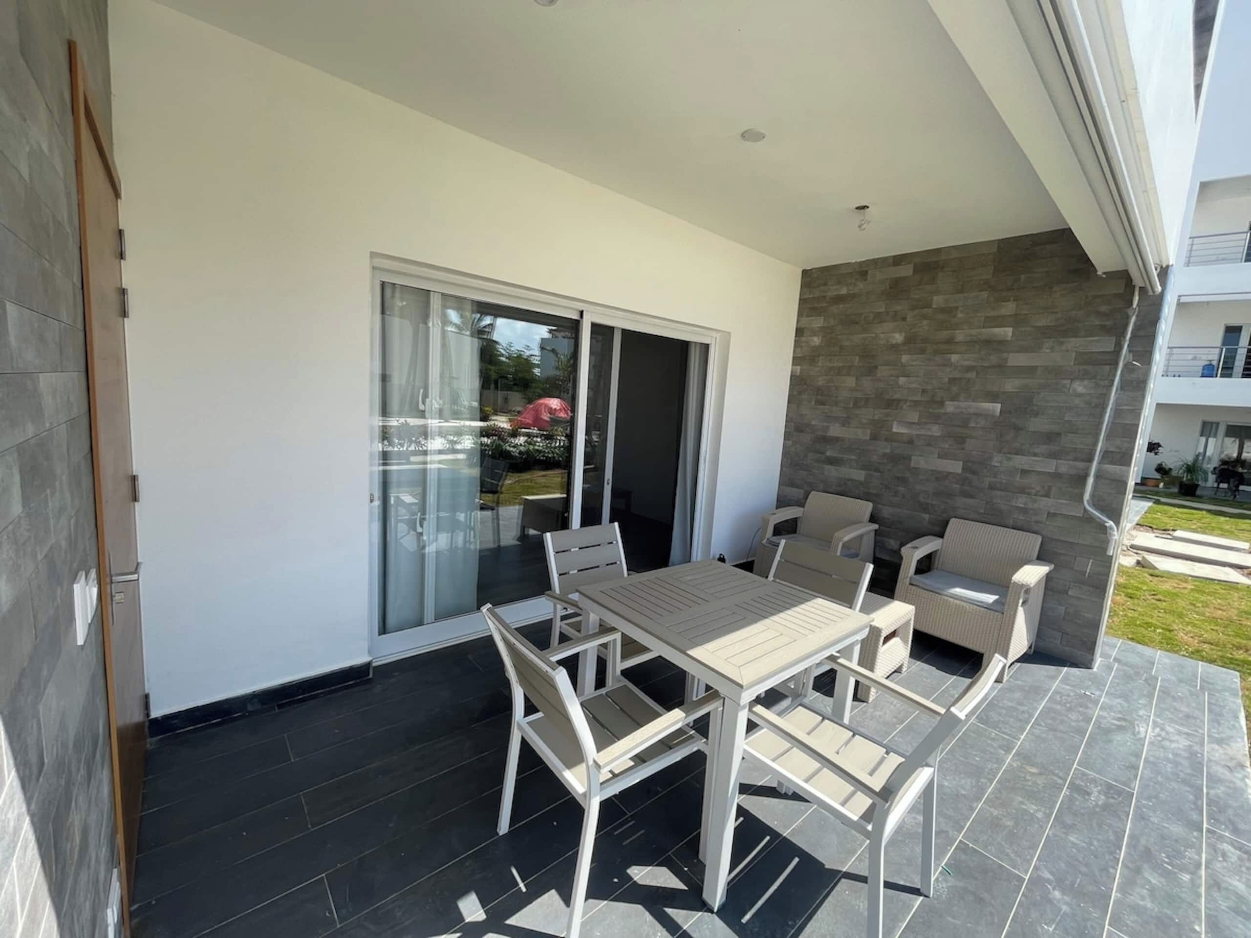 A modern outdoor patio with a dining table and chairs, a sliding glass door, and a stone wall.