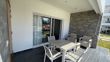 A modern outdoor patio with a dining table and chairs, a sliding glass door, and a stone wall.