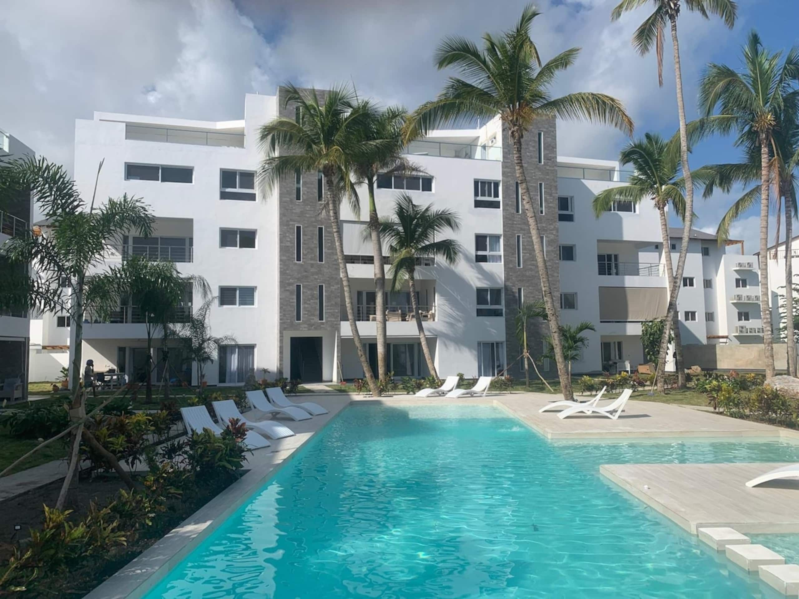 Un hôtel moderne doté d’une piscine, de palmiers et de chaises longues.