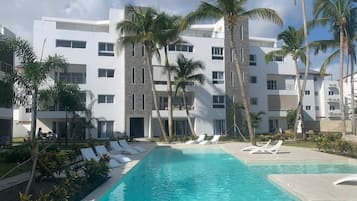Un hôtel moderne doté d’une piscine, de palmiers et de chaises longues.