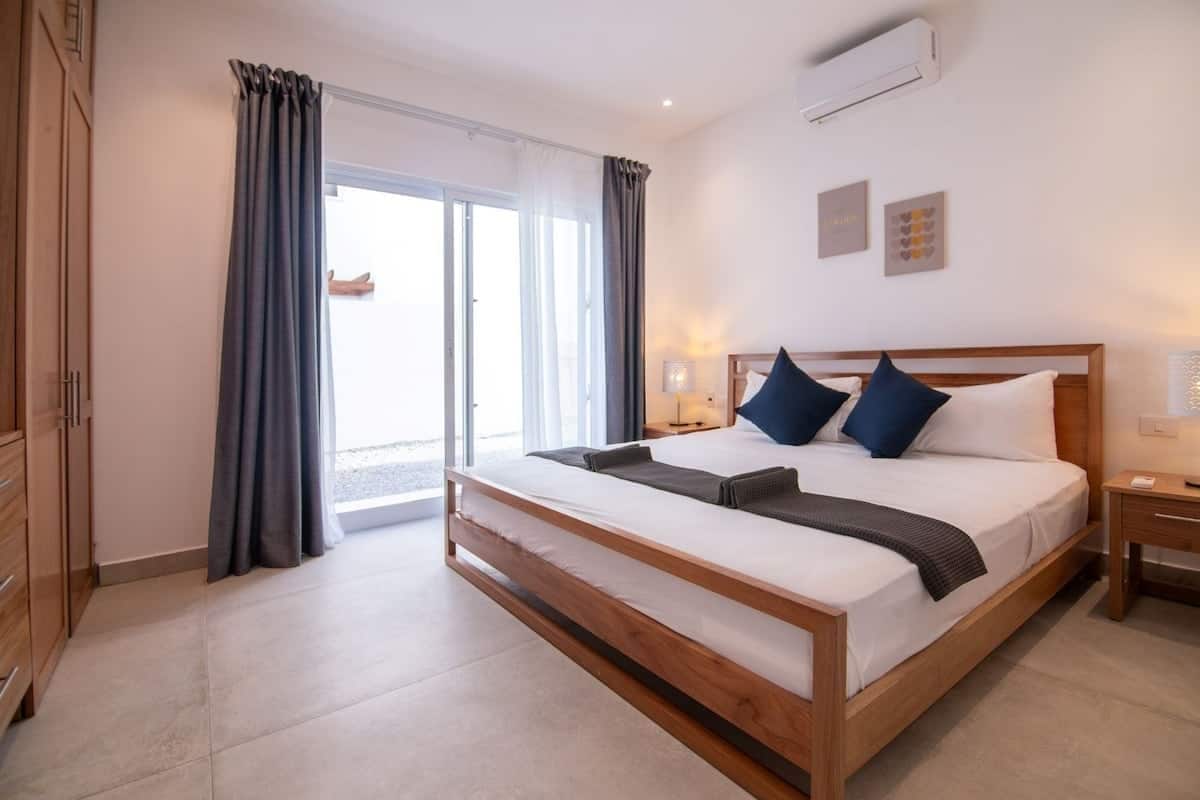 A modern bedroom with a wooden bed, a nightstand, a bedside table, and a view through a glass door to the outside.