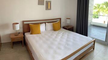 A hotel room with a large bed, two bedside tables, a lamp, a wall-mounted air conditioner, and a view of the outdoors.