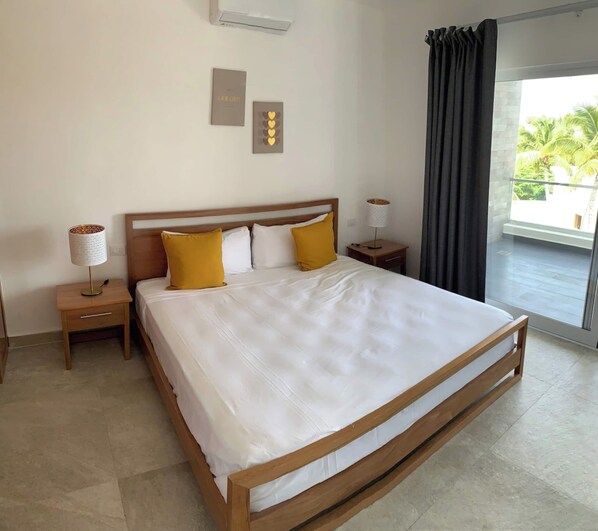 Habitación de hotel con una cama grande, dos mesitas de noche, una lámpara, aire acondicionado instalado en la pared y vista al exterior.