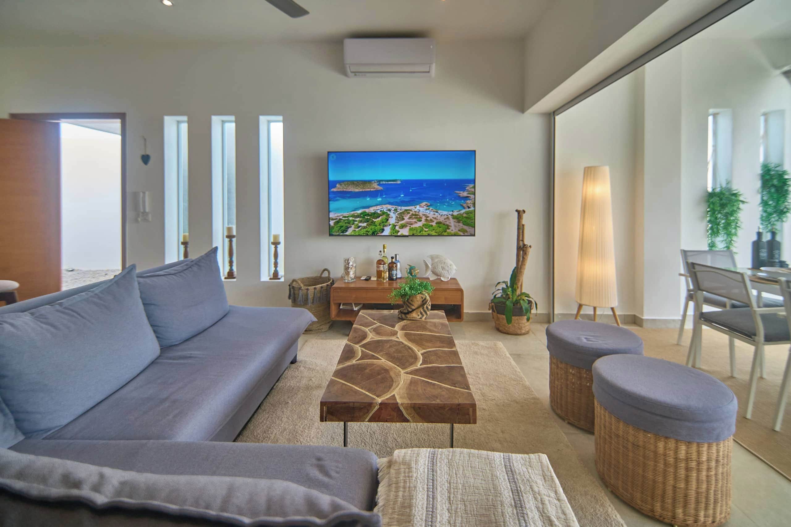 Un salón moderno con un sofá gris, una mesa de centro, un televisor montado en la pared y vista al mar.