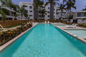 A rectangular swimming pool with clear blue water, surrounded by white lounge chairs and palm trees. - Case Damare Coralstone 3 (Las terrenas)