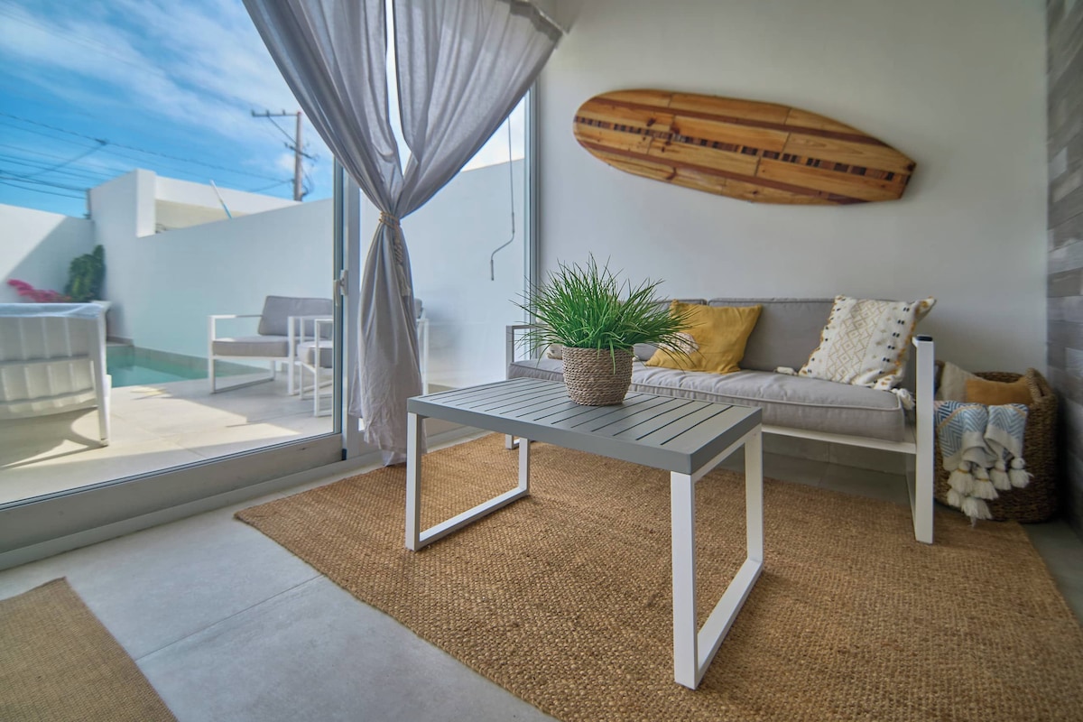 Una sala de estar moderna con un sofá, una mesa con una planta y una tabla de surf en la pared.