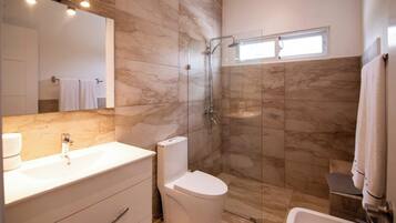 A modern bathroom with a marble wall, a glass shower enclosure, a white toilet, and a sink with a mirror above it.