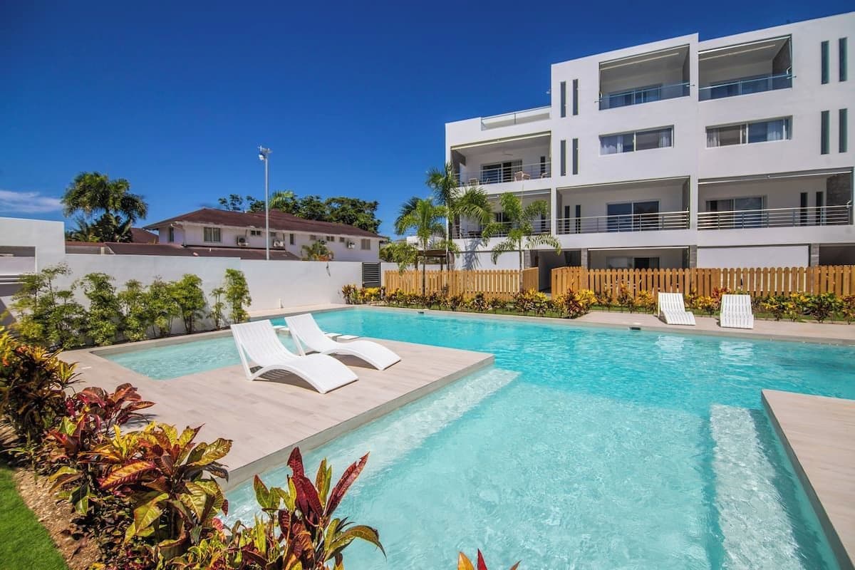A modern building with a swimming pool, lounge chairs, and a wooden fence.