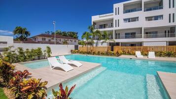 A modern building with a swimming pool, lounge chairs, and a wooden fence.