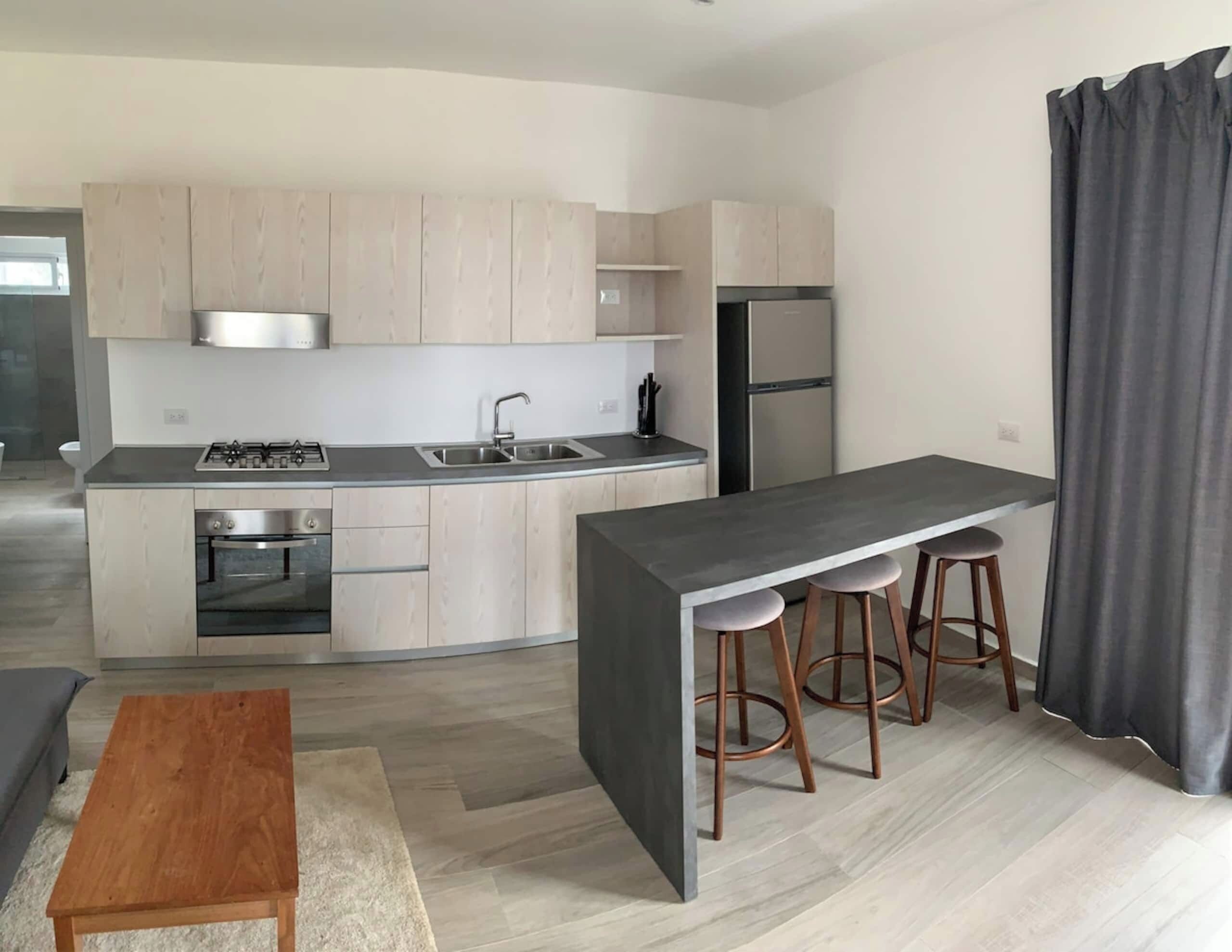 Een moderne keuken met een centraal eiland, roestvrijstalen apparatuur en licht houten kasten.