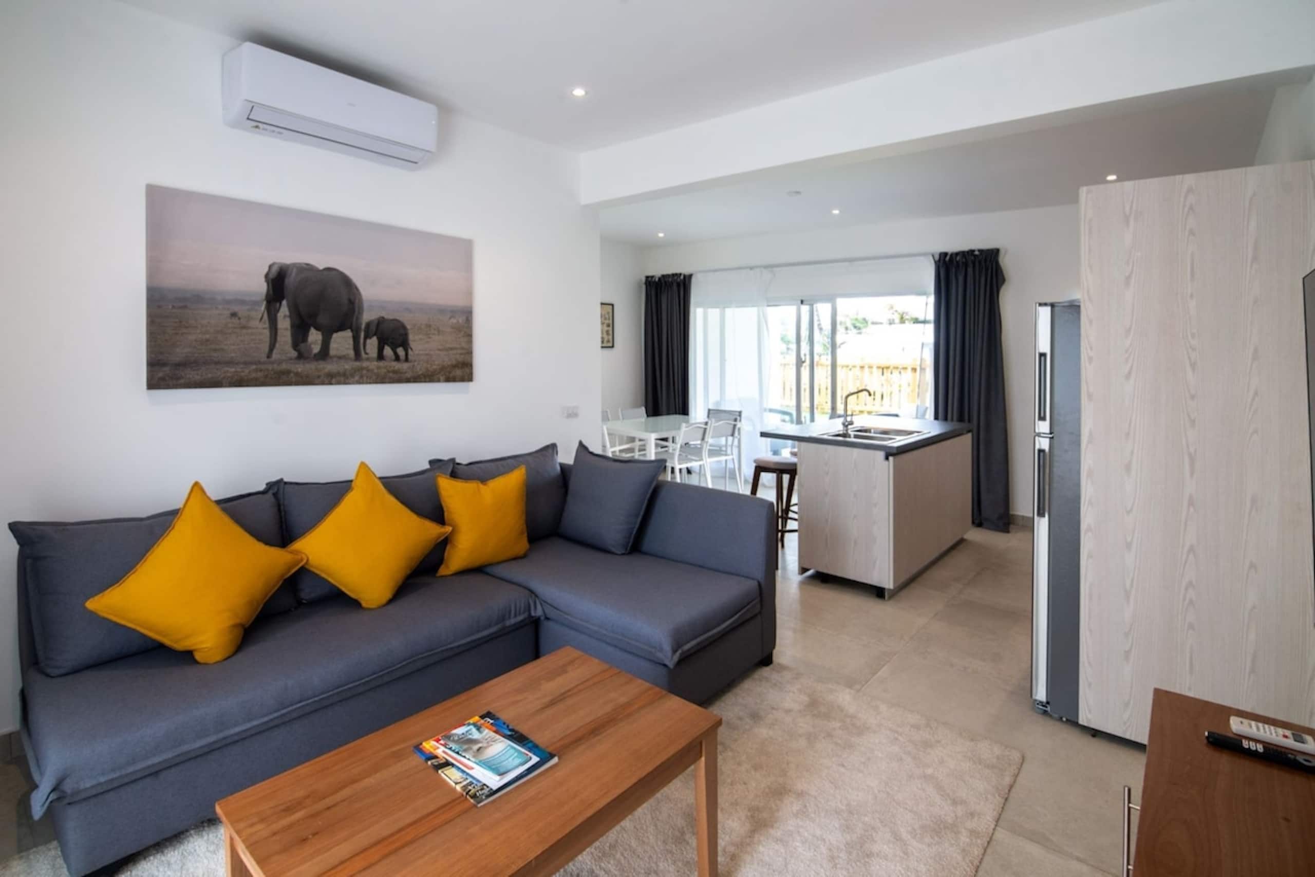A modern living room with a grey sofa, wooden coffee table, and a painting of elephants.