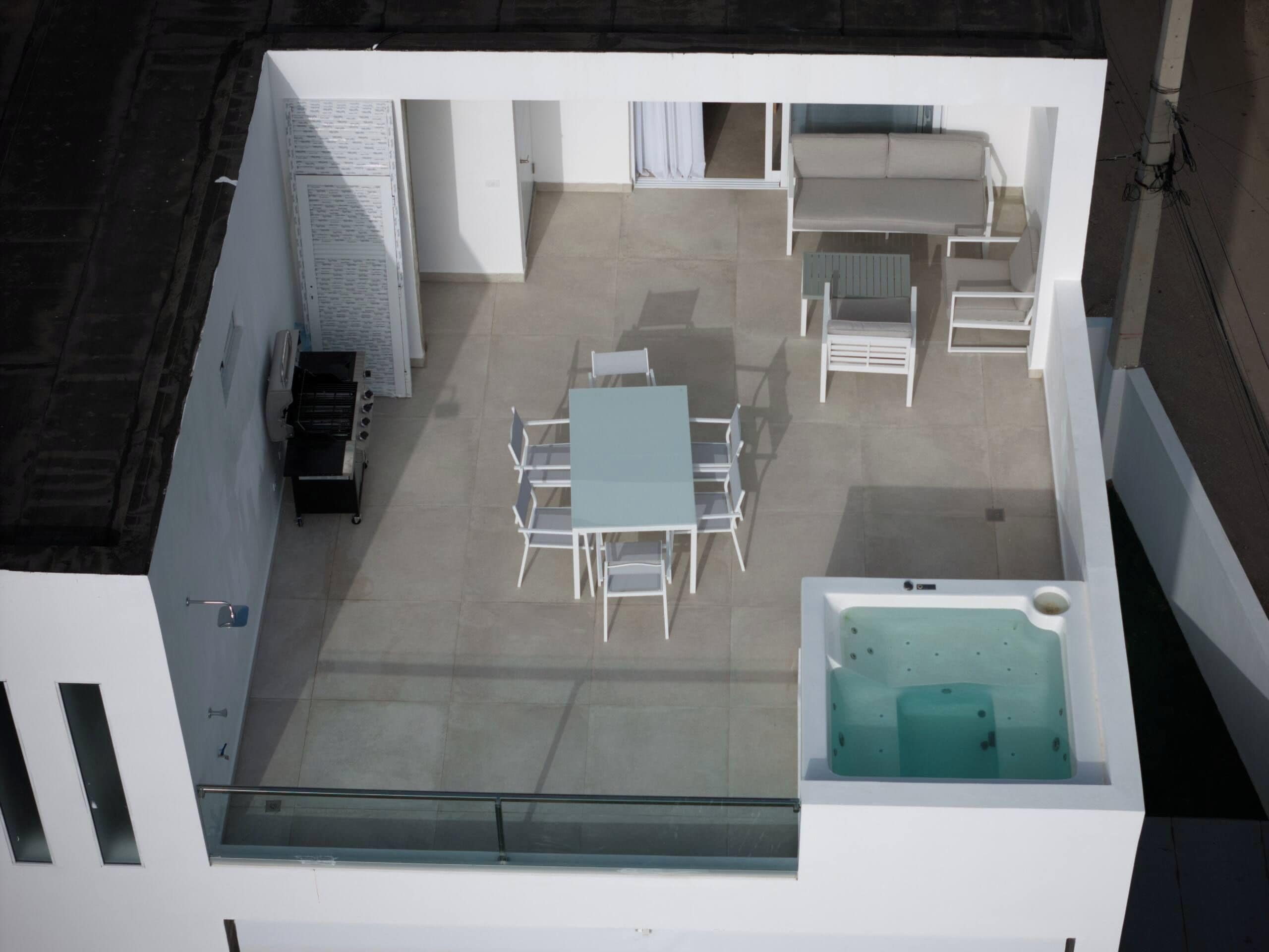 A rooftop terrace with a table and chairs, a sofa, a hot tub, and a grill.