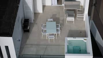 A rooftop terrace with a table and chairs, a sofa, a hot tub, and a grill.