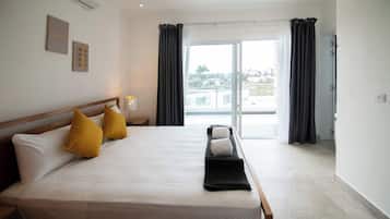 Ein Hotelzimmer mit Bett, Kissen, Nachttisch, Lampe und Blick ins Freie.