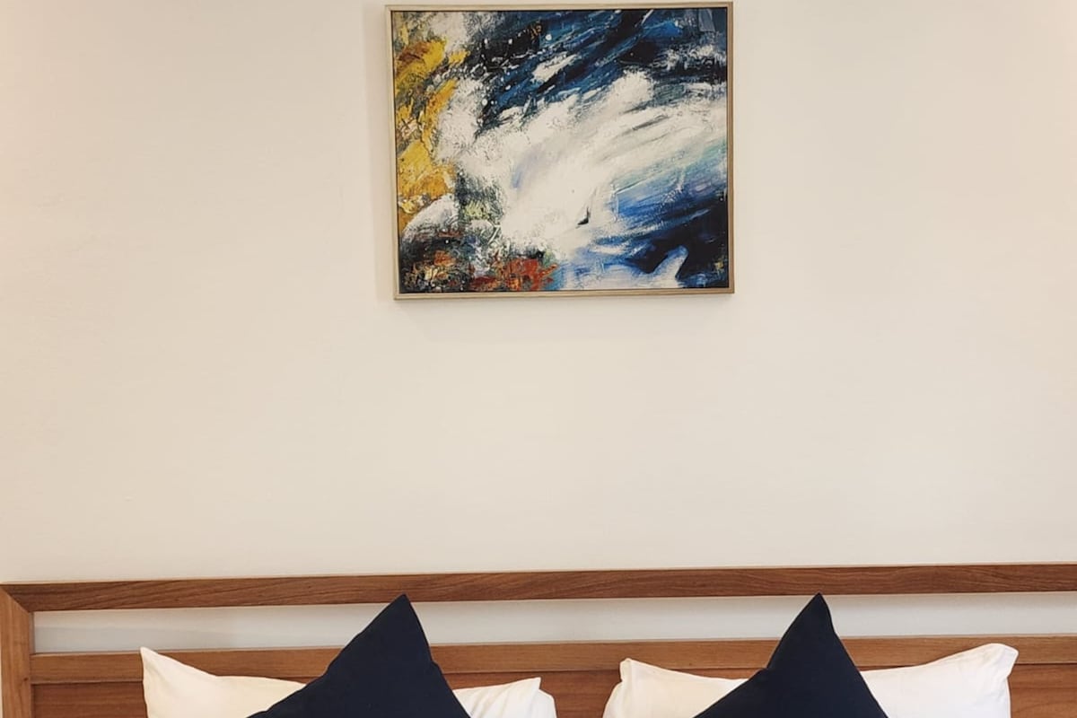 Habitación de hotel con cama, dos almohadas, una colcha y un cuadro en la pared.