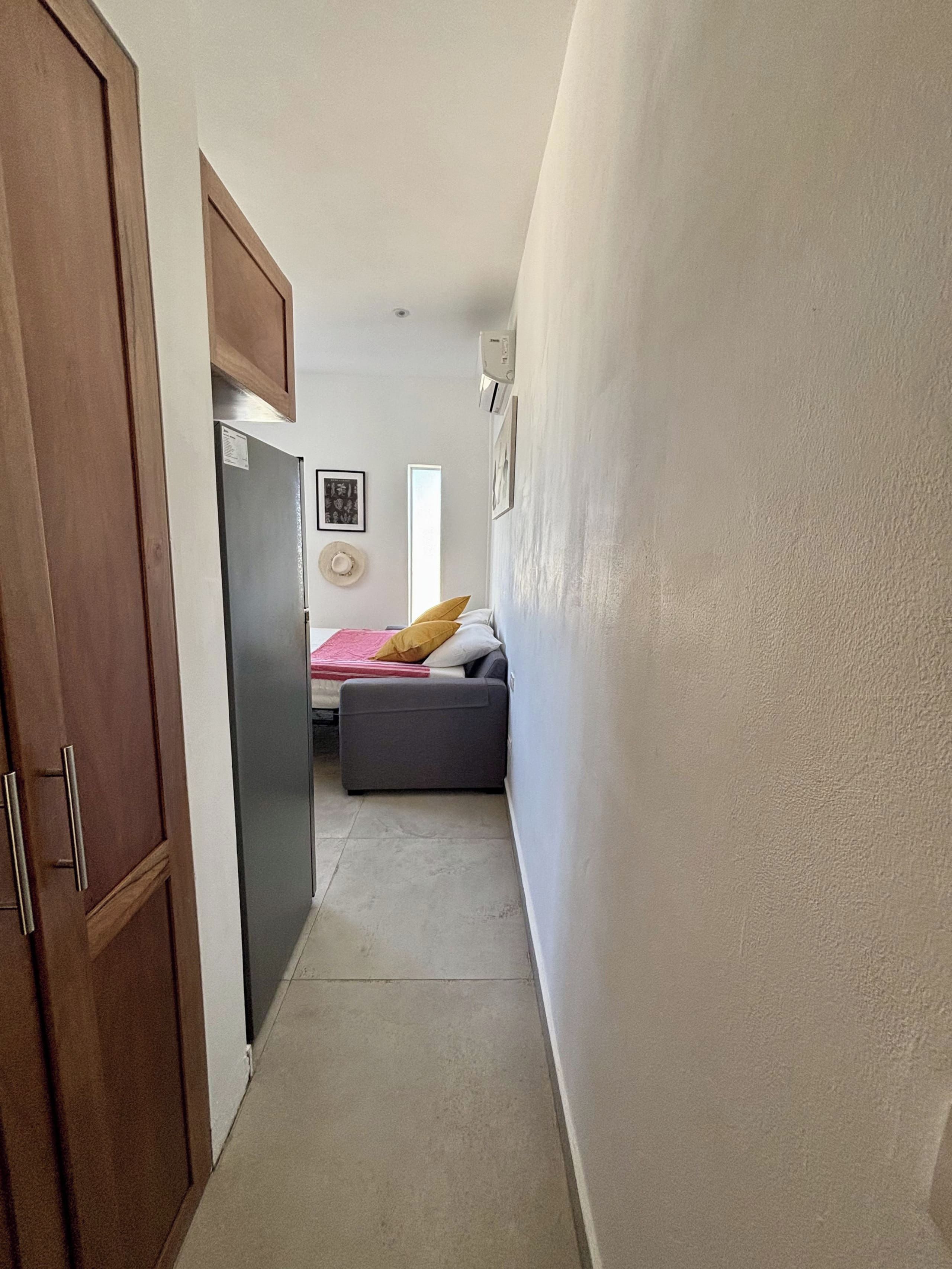 A narrow hallway leading to a bedroom with a bed, a wardrobe, and a wall-mounted air conditioner.