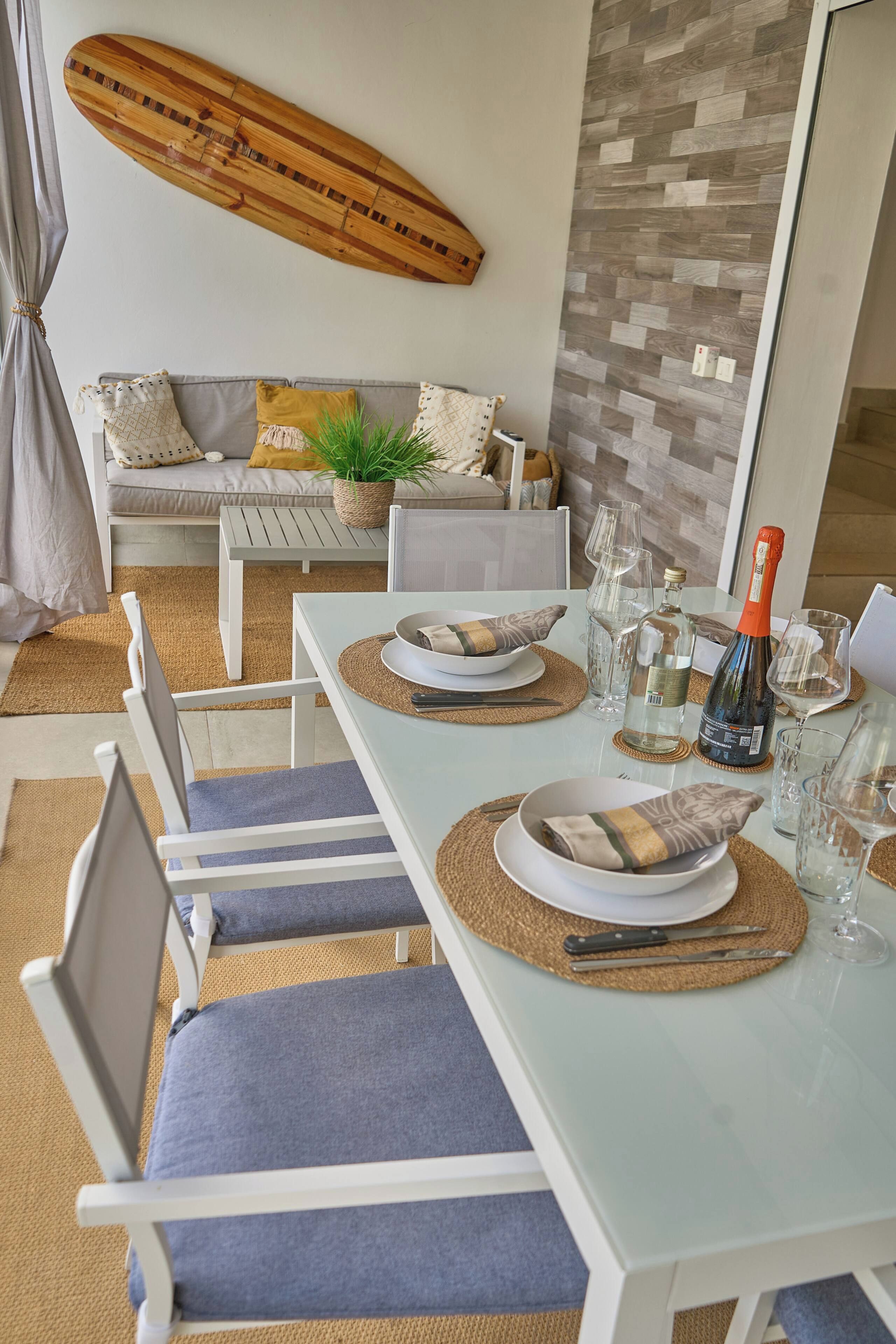 A dining area with a white table set for two, including plates, bowls, cutlery, and glasses.