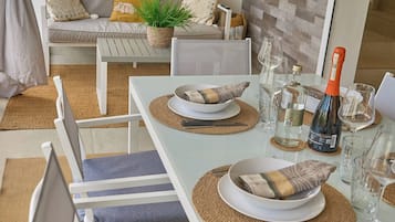 A dining area with a white table set for two, including plates, bowls, cutlery, and glasses.