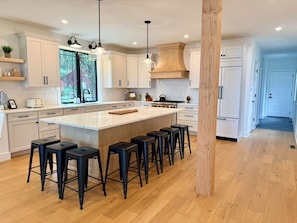 A modern kitchen with a large island, bar stools, and wooden flooring.