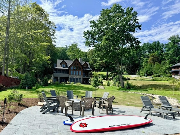 A patio with lounge chairs and a surfboard, a house in the background, and a well-maintained lawn.
