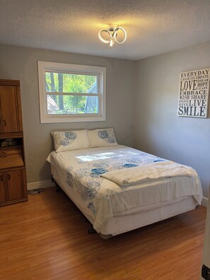 A bedroom with a bed, a window, a wooden cabinet, and a motivational quote on the wall.