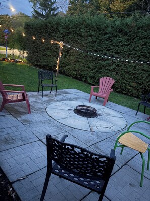 Een terras met vuurkorf, buitenmeubels en sfeerverlichting.