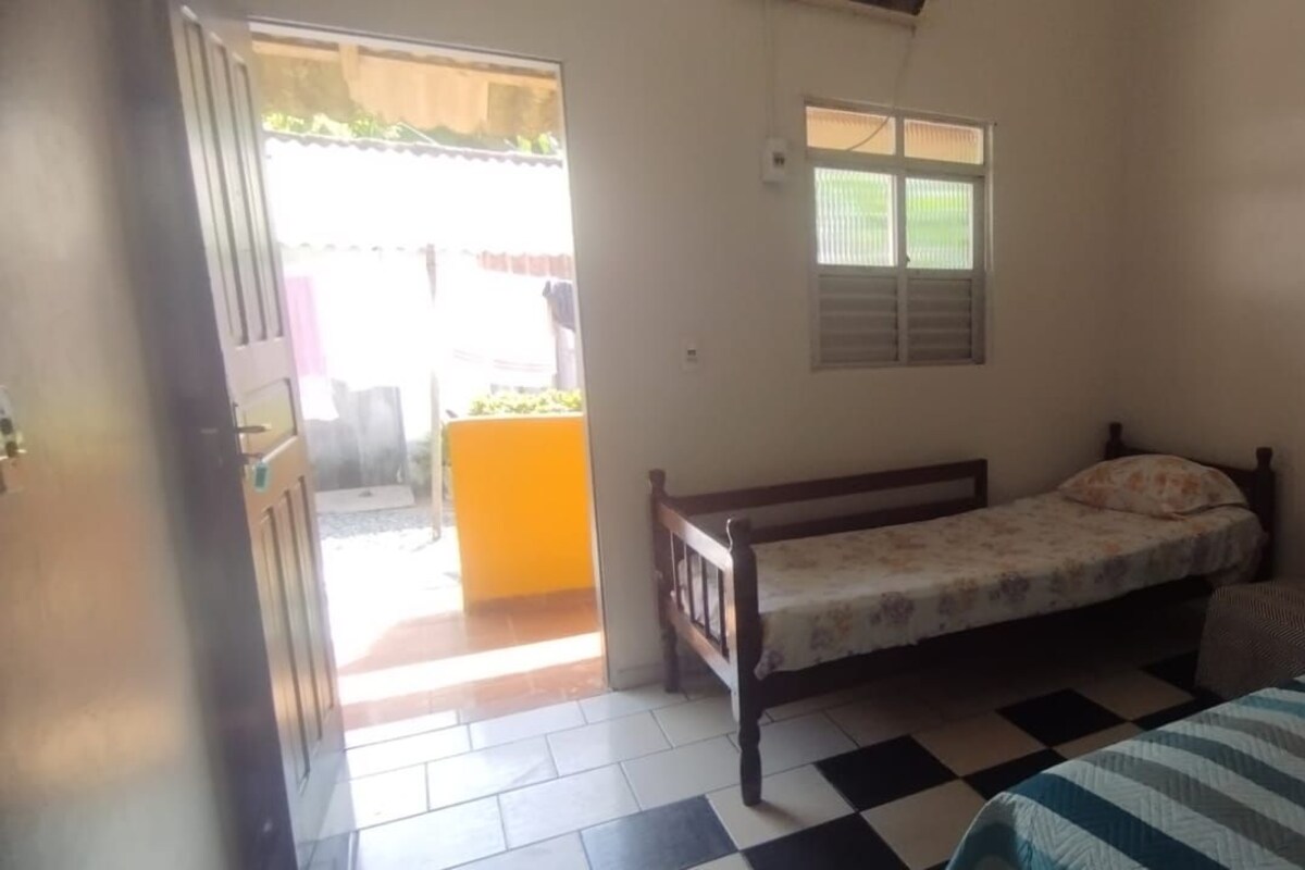 A room with a bed, a chair, a small table, a window, and a door leading outside.