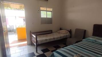 A room with a bed, a chair, a small table, a window, and a door leading outside.