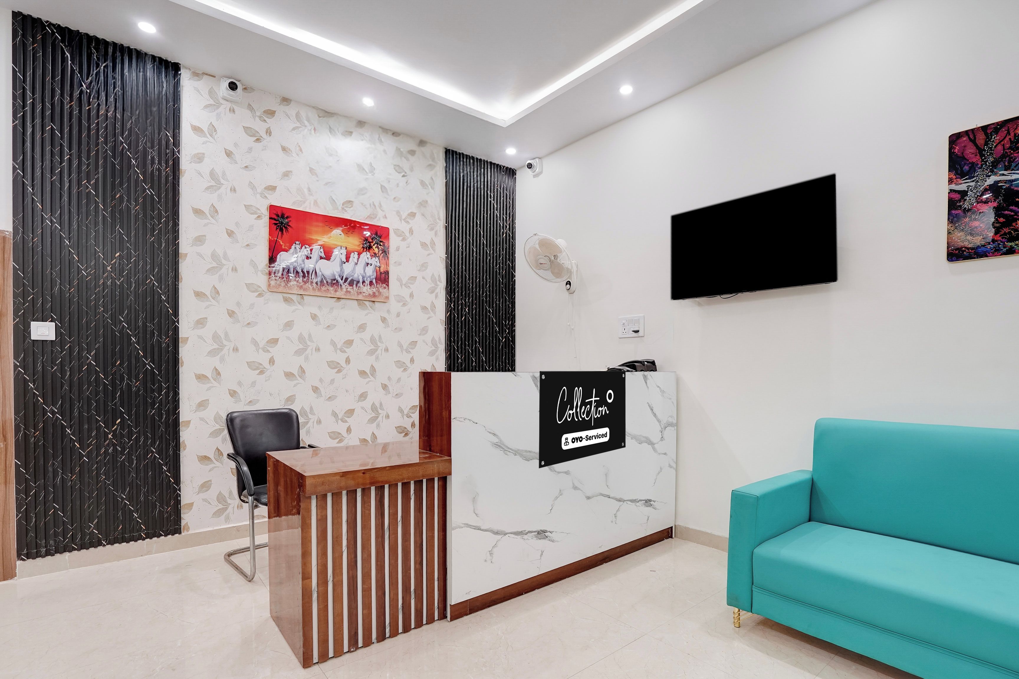 A reception area with a wooden desk, a teal sofa, a mounted TV, and a wall with a floral pattern and a framed picture.