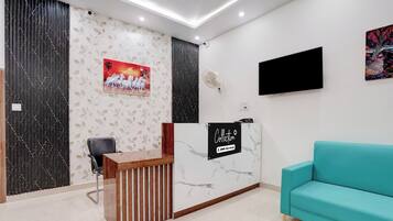 A reception area with a wooden desk, a teal sofa, a mounted TV, and a wall with a floral pattern and a framed picture.