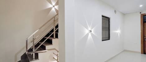 Una escalera con barandilla metálica que lleva a un rellano, una lámpara fijada a la pared y una puerta con ventanal.