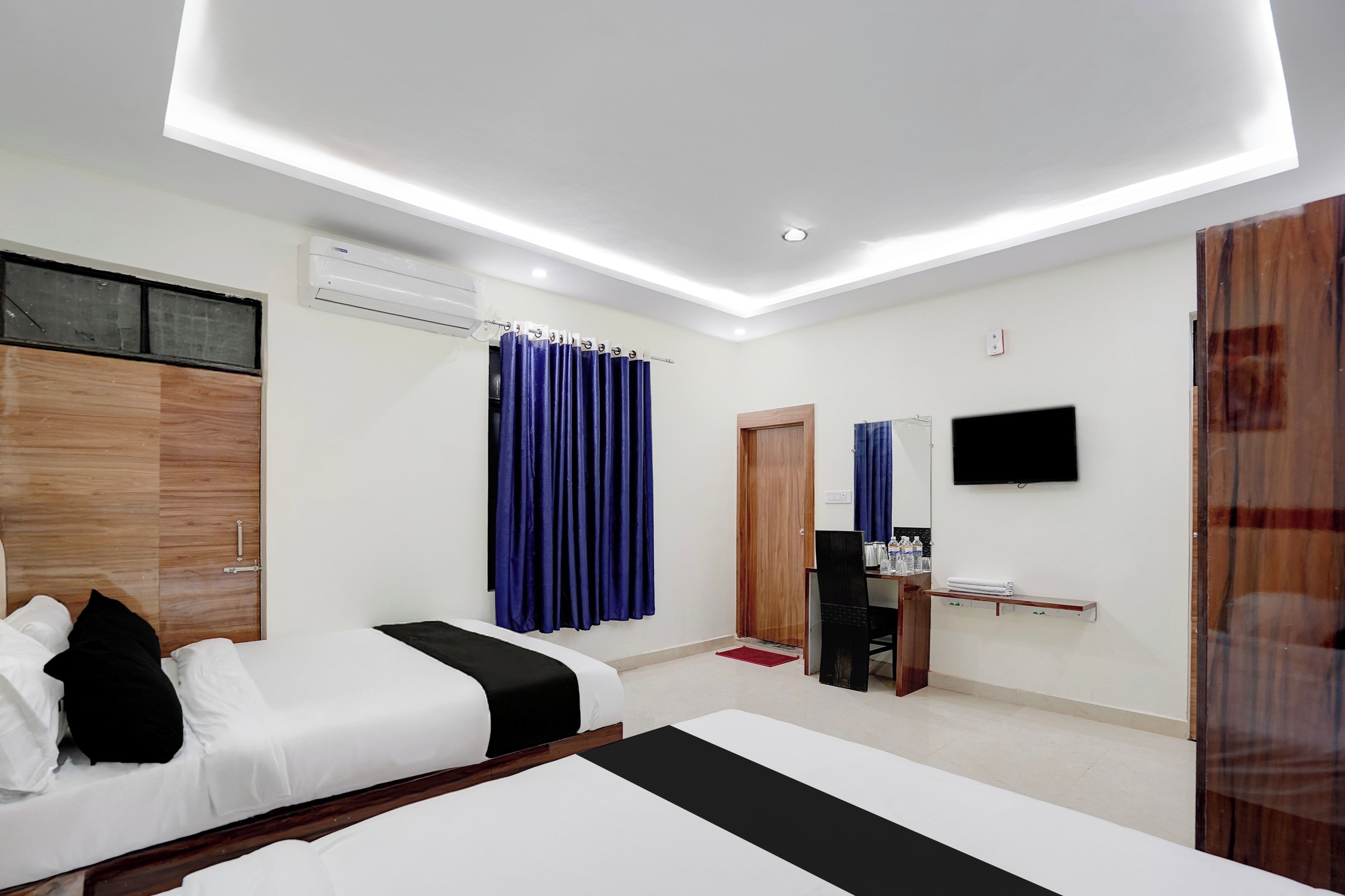 A hotel room with two beds, a flat-screen TV, an air conditioning unit, and a wooden wardrobe.