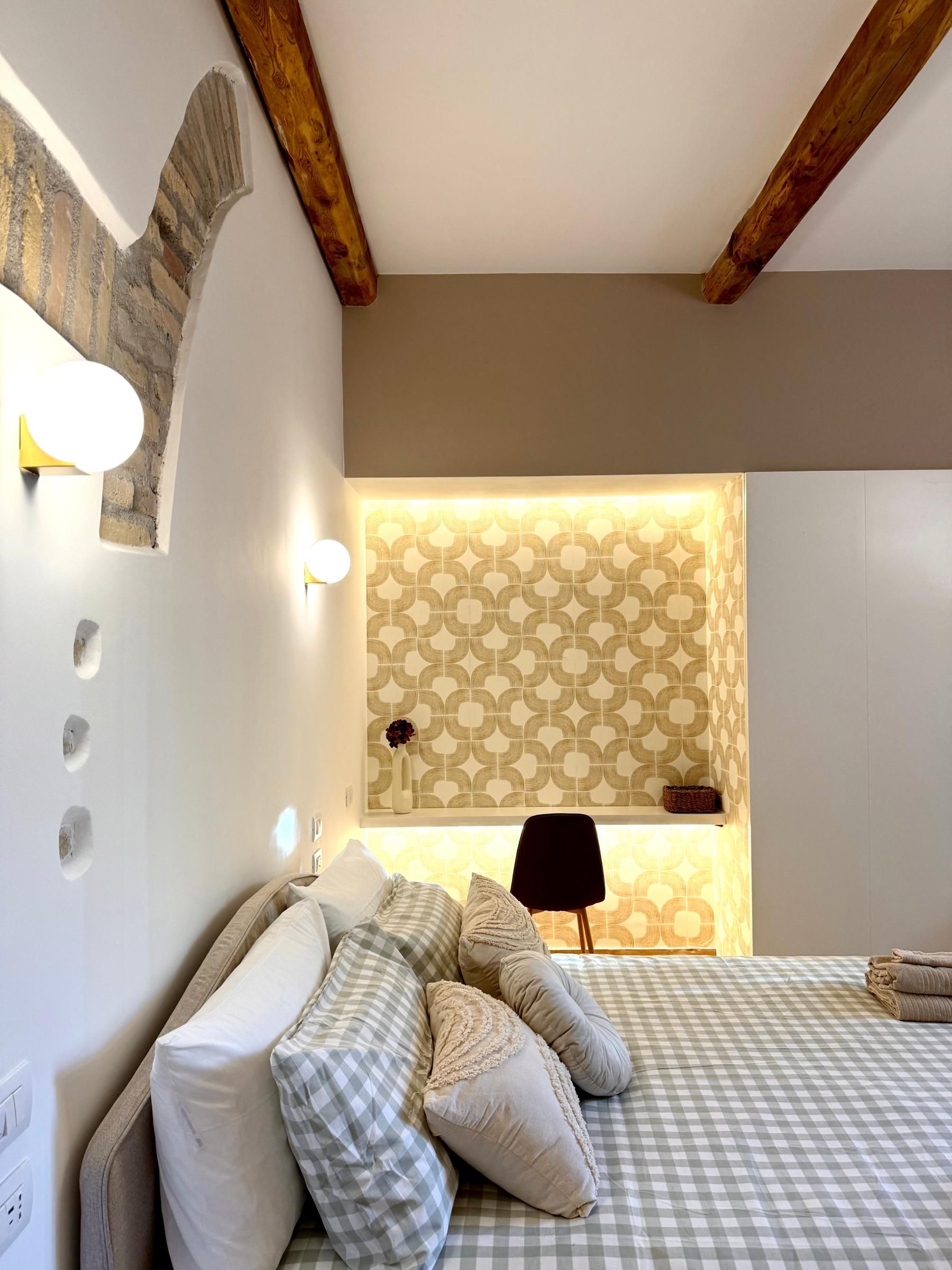 Une chambre à coucher avec une couvre-lit à carreaux, une table de chevet avec une lampe et un mur orné d’un motif géométrique.