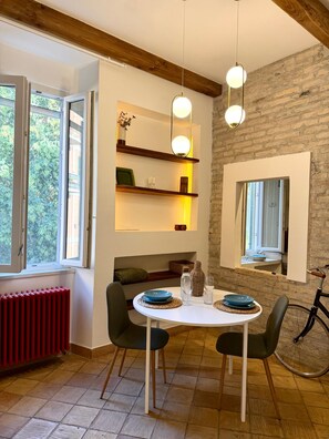 Un coin repas avec une table dressée pour deux personnes, un radiateur rouge et un vélo posé dans un coin.