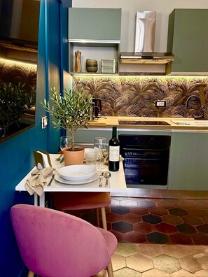 A modern kitchen with a dining area, a potted plant, and a wine bottle on the table. - LIVING ROOM 18 - KING COMFORT ROOM (ROMA)