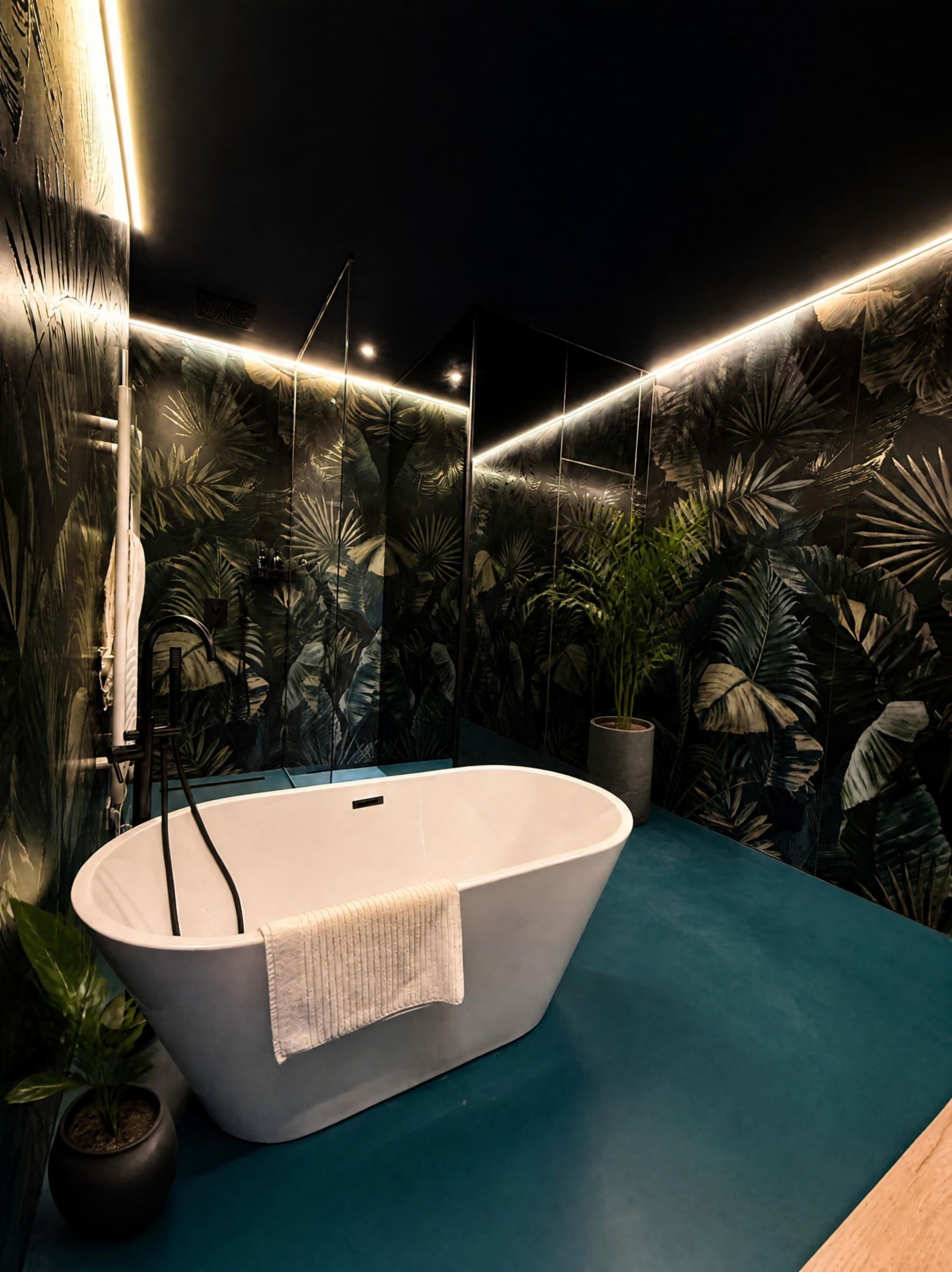 Un bagno moderno con una vasca freestanding, un pavimento blu e una parete decorata con murales di piante tropicali.
