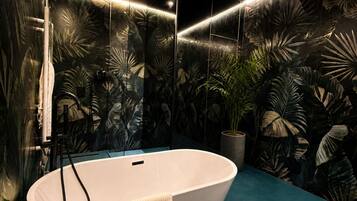 Un bagno moderno con una vasca freestanding, un pavimento blu e una parete decorata con murales di piante tropicali.