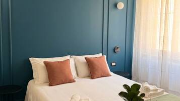 Una camera da letto con un letto, cuscini, un comodino con una pianta e una finestra con tende.