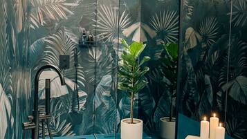 Un bagno moderno con una vasca freestanding, una pianta in vaso e uno specchio con motivo a foglia tropicale.