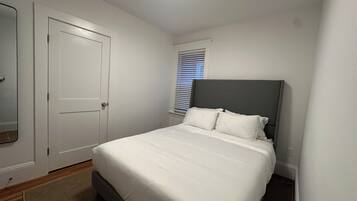 Une chambre à coucher avec un lit, une porte, une fenêtre avec des stores et un luminaire au plafond.