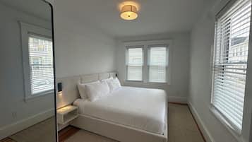 A bedroom with a bed, a nightstand, a mirror, and a ceiling light fixture.