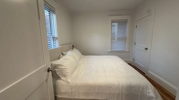 A bedroom with a bed, two windows with blinds, a door, and a ceiling light fixture.